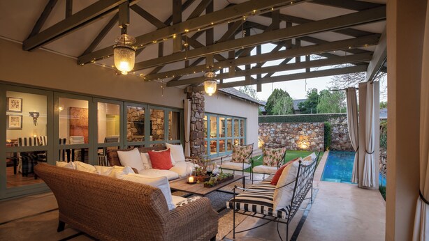 Cómoda zona de estar interior con mobiliario de mimbre, una pared de piedra y vista a una piscina.