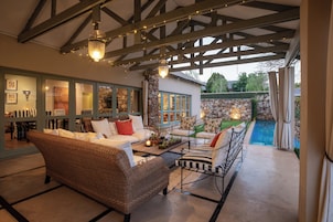 Cómoda zona de estar interior con mobiliario de mimbre, una pared de piedra y vista a una piscina.