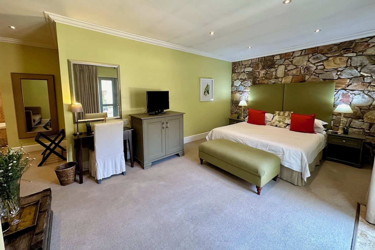 A bedroom with a bed, a desk, a chair, a television, and a stone wall.