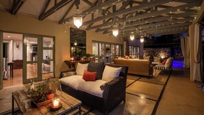 Un espacio al aire libre con mobiliario de mimbre, una mesa de madera con vela y luces colgantes.