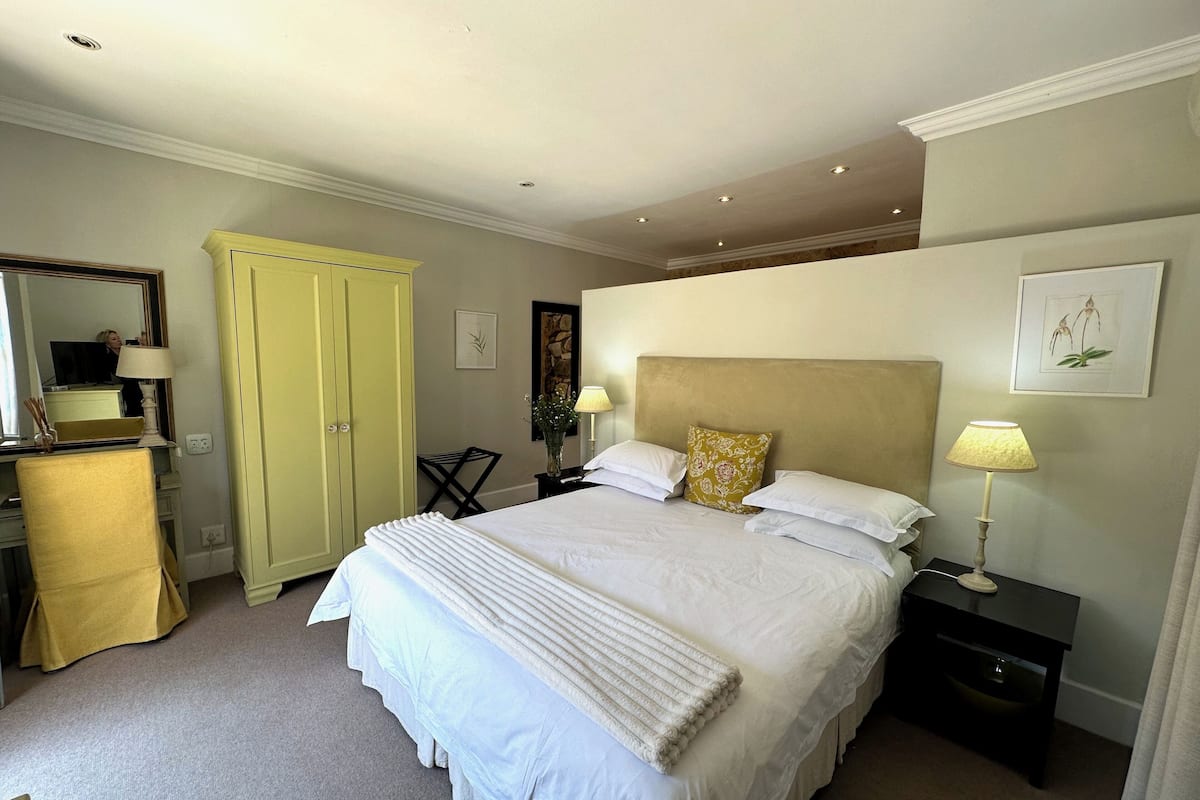 A neatly arranged bedroom with a large bed, bedside tables, a wardrobe, and a mirror.