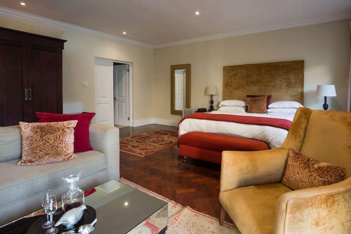 A hotel room with a bed, a sofa, a chair, a coffee table, and a large mirror.