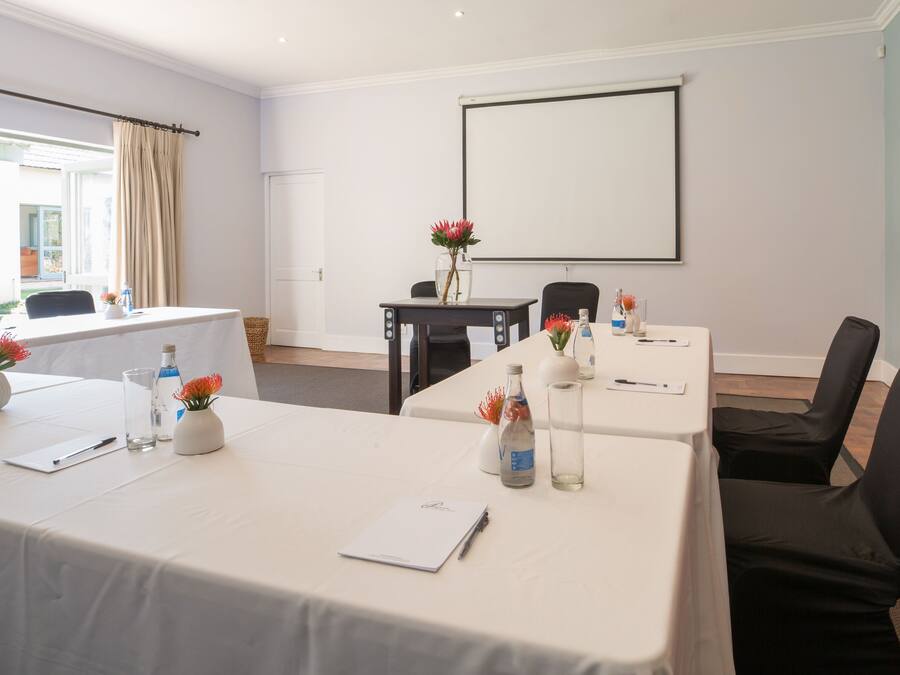 A conference room with a white table, black chairs, a projector screen, and a window with curtains.