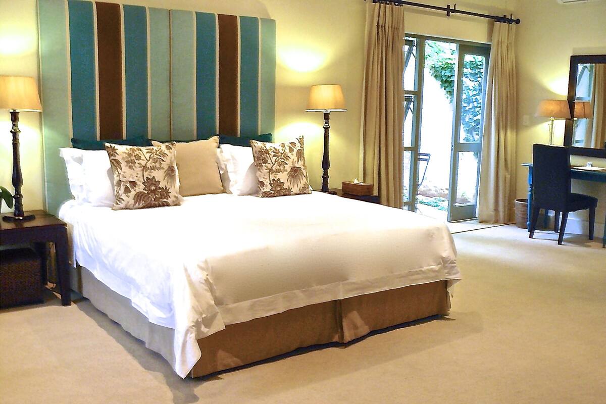 A large bed with white linens, flanked by two bedside tables with lamps, a striped wall, and a view of the outdoors through a glass door.