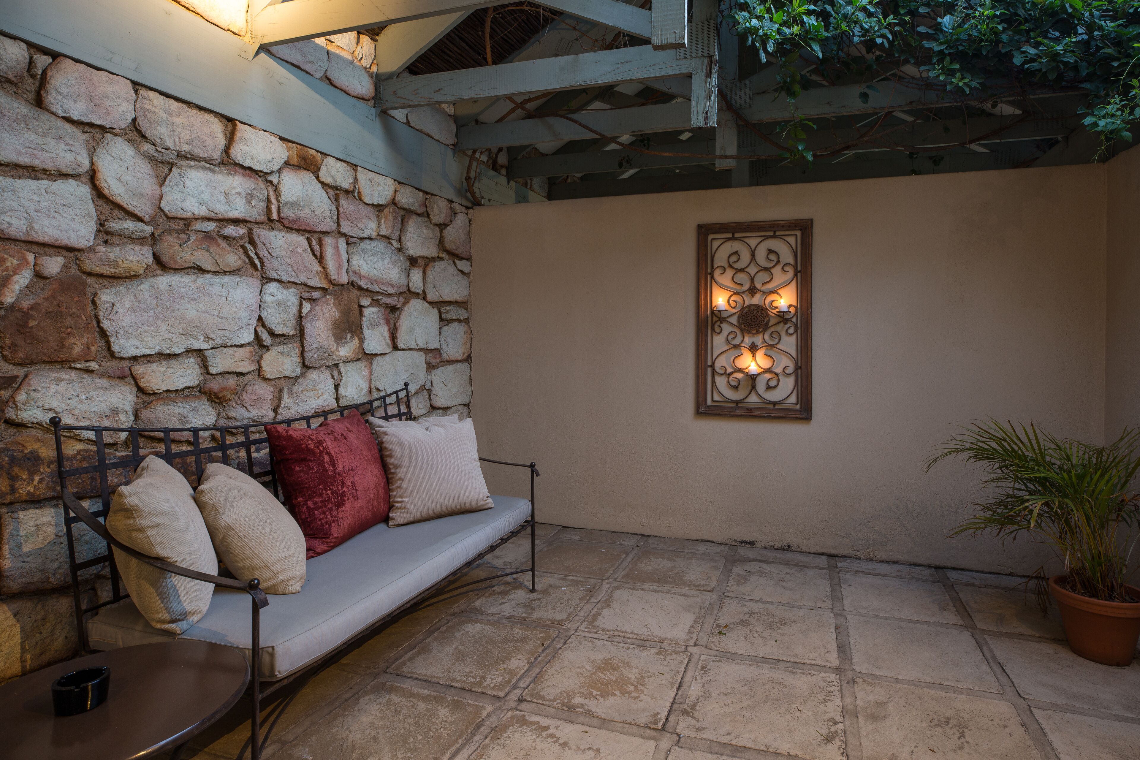 A stone wall, a metal bench with cushions, a potted plant, and a decorative wall piece.