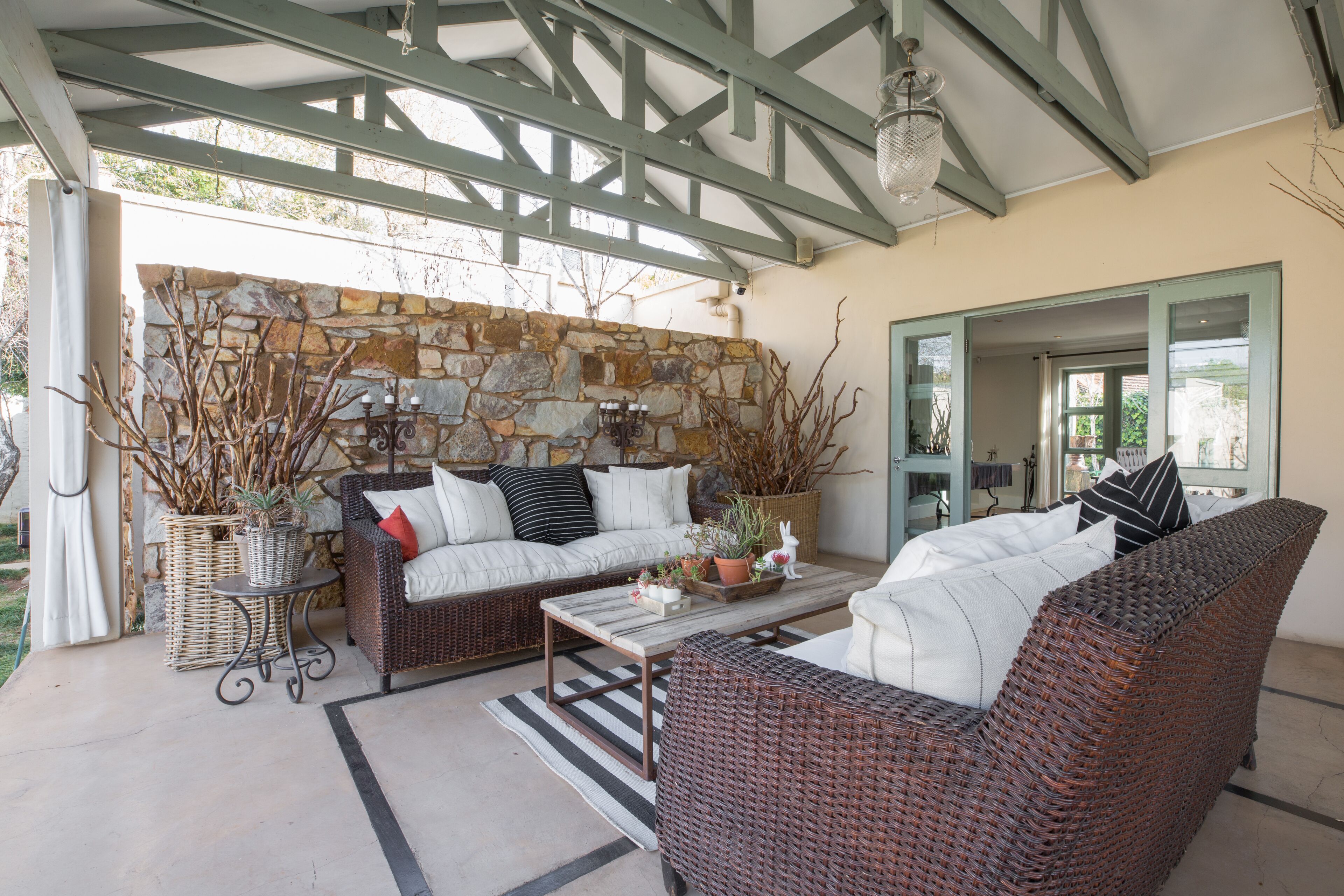 A covered outdoor seating area with wicker furniture, stone wall, and a view of the outdoors.