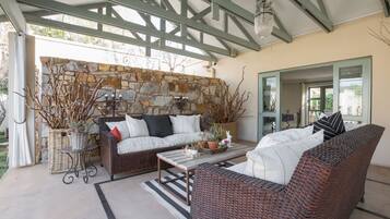 A covered outdoor seating area with wicker furniture, stone wall, and a view of the outdoors.