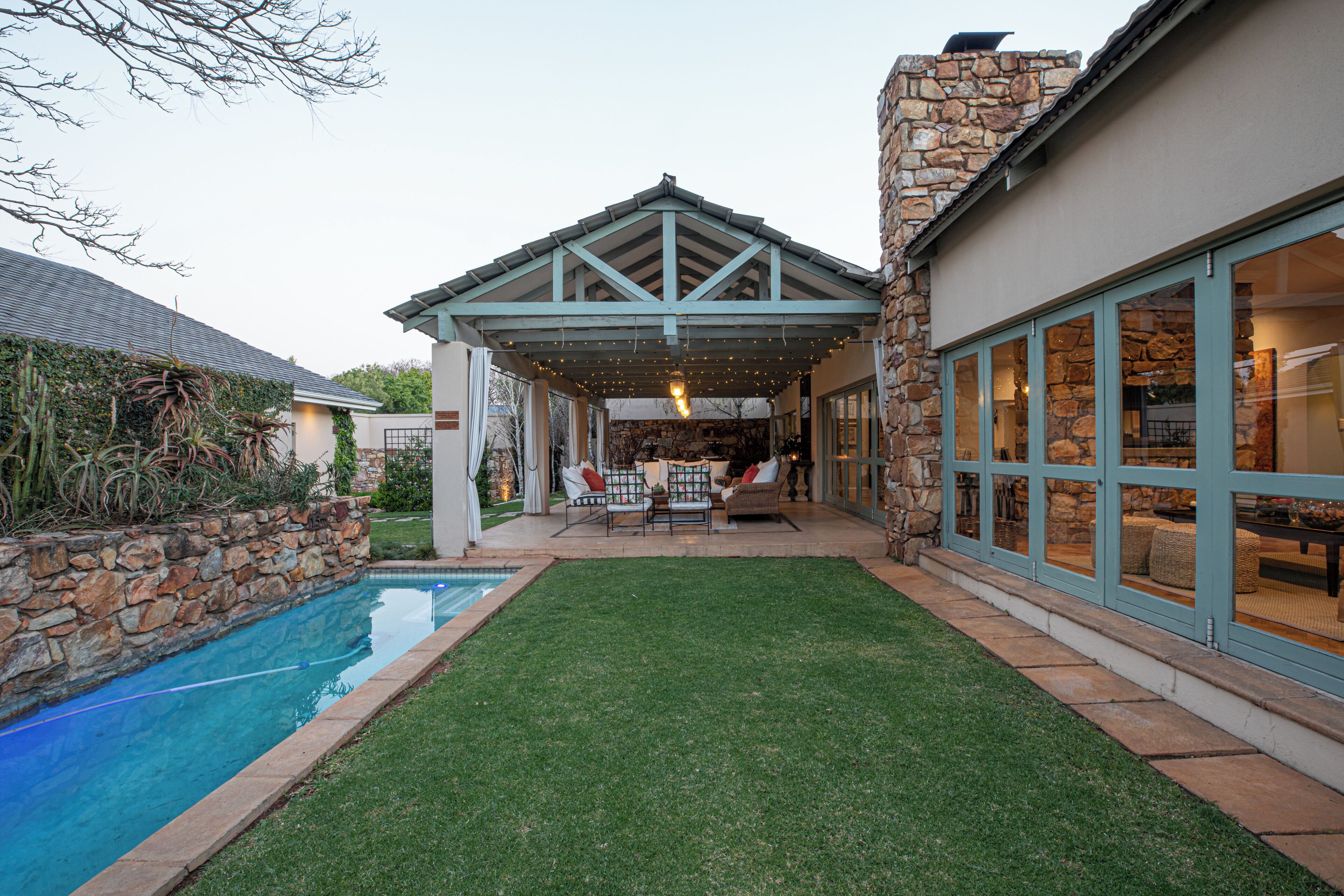 A poolside patio with a covered seating area, stone walls, and a clear view of the pool.