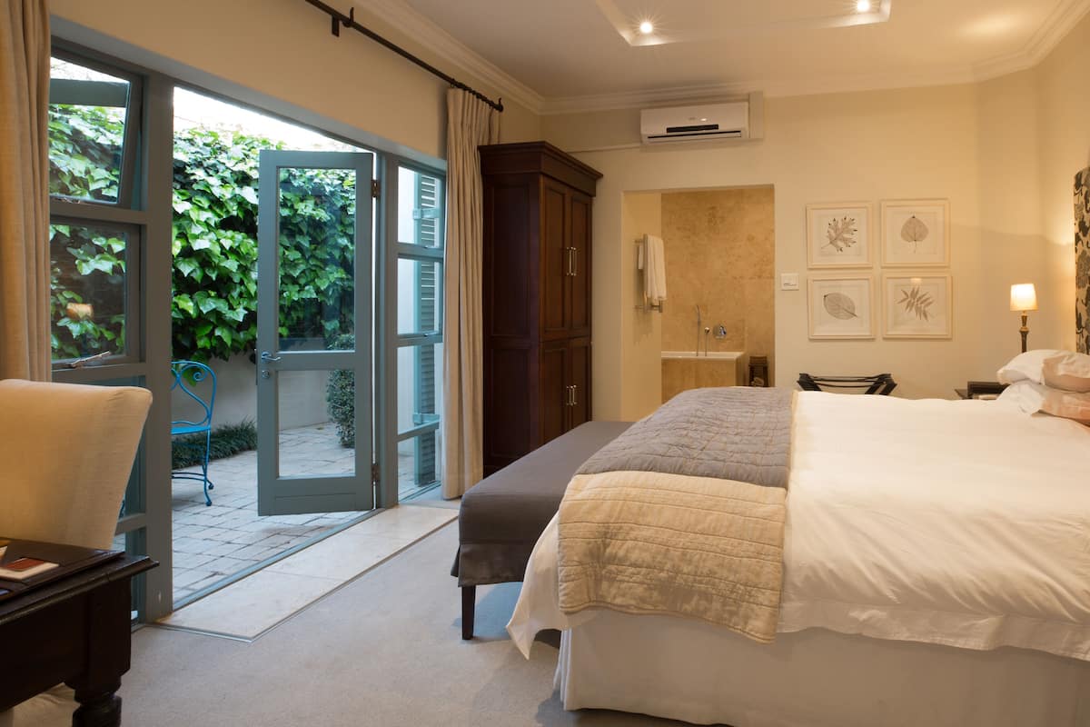 A bedroom with a bed, a desk, a chair, a bathroom, and a view of the outdoors.