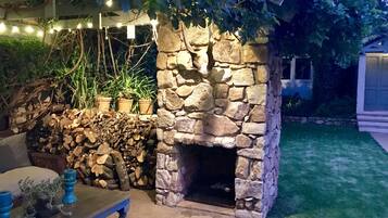 A stone fireplace with a rustic design, surrounded by a stone wall and potted plants.