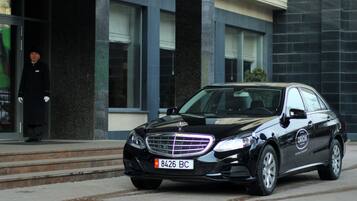 Een zwarte Mercedes-Benz geparkeerd voor een gebouw met een glazen ingang en een trap.