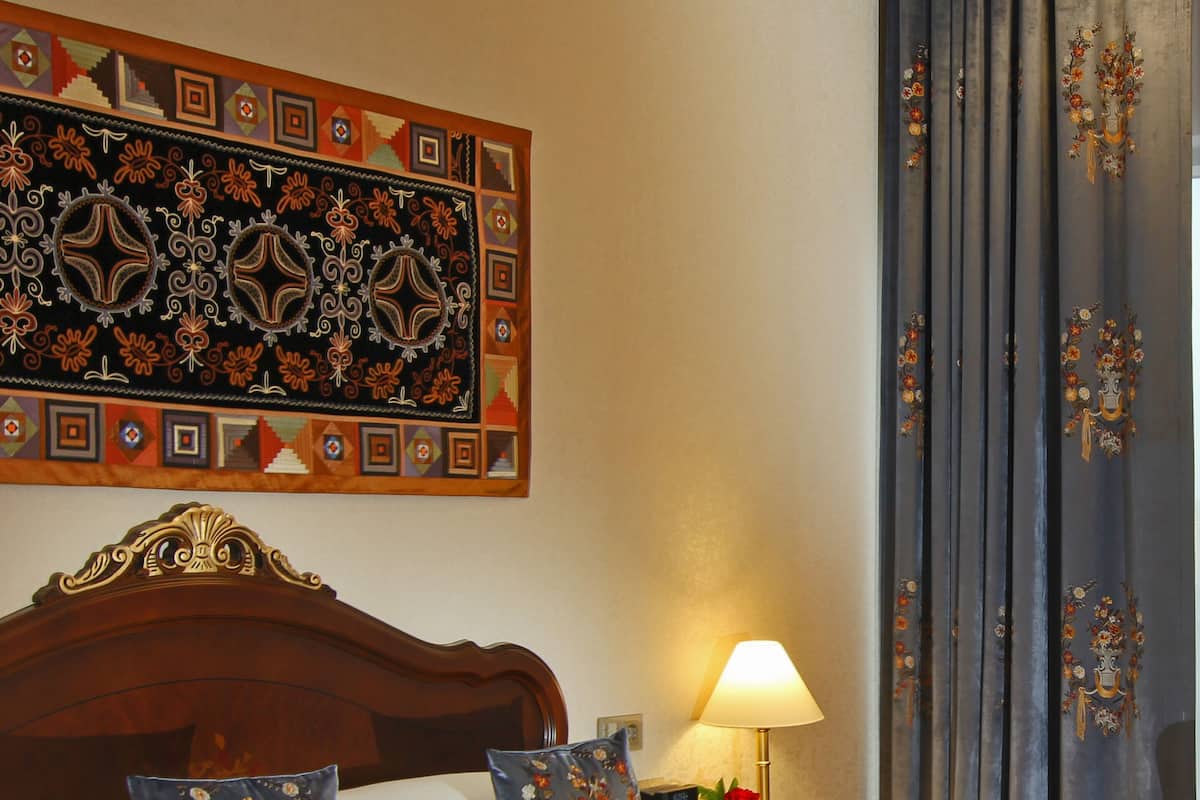 Een net opgemaakt bed met bloemenkussens, een houten hoofdbord en een nachtkastje met een lamp.
