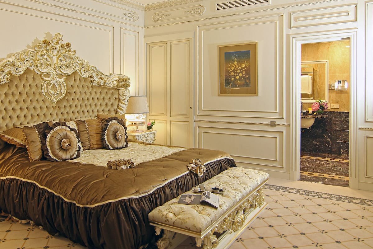 Een luxueuze slaapkamer met een gebordureerd hoofdeinde, versierde beddengoed en een klassiek design.