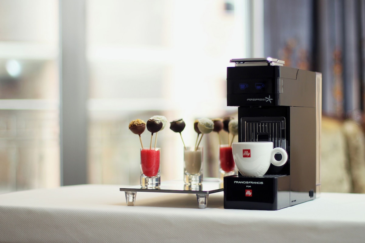 Eine Kaffeemaschine mit Tasse und einem Glas roter Flüssigkeit auf einem Tisch.
