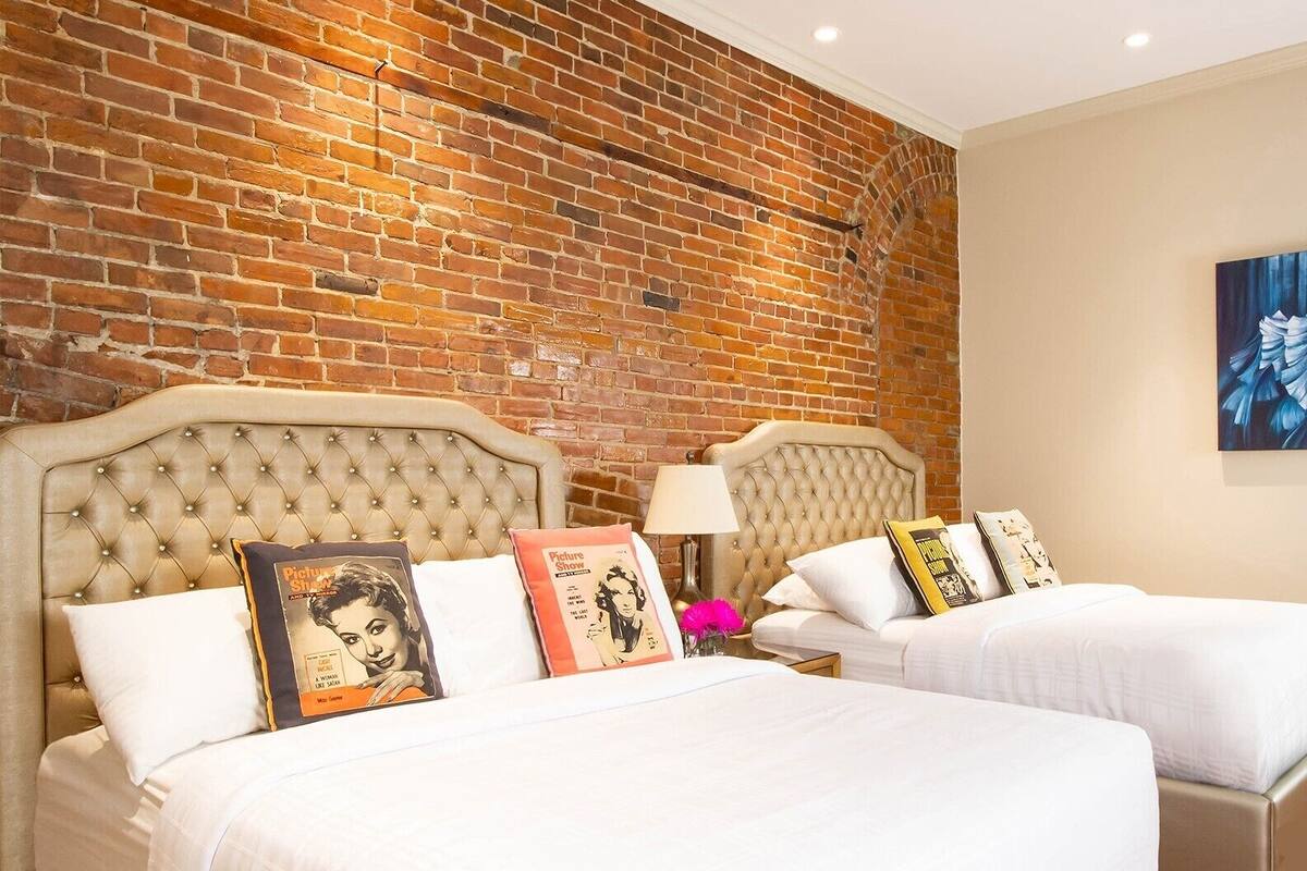 A hotel room with two beds, a brick wall, and a painting on the wall.