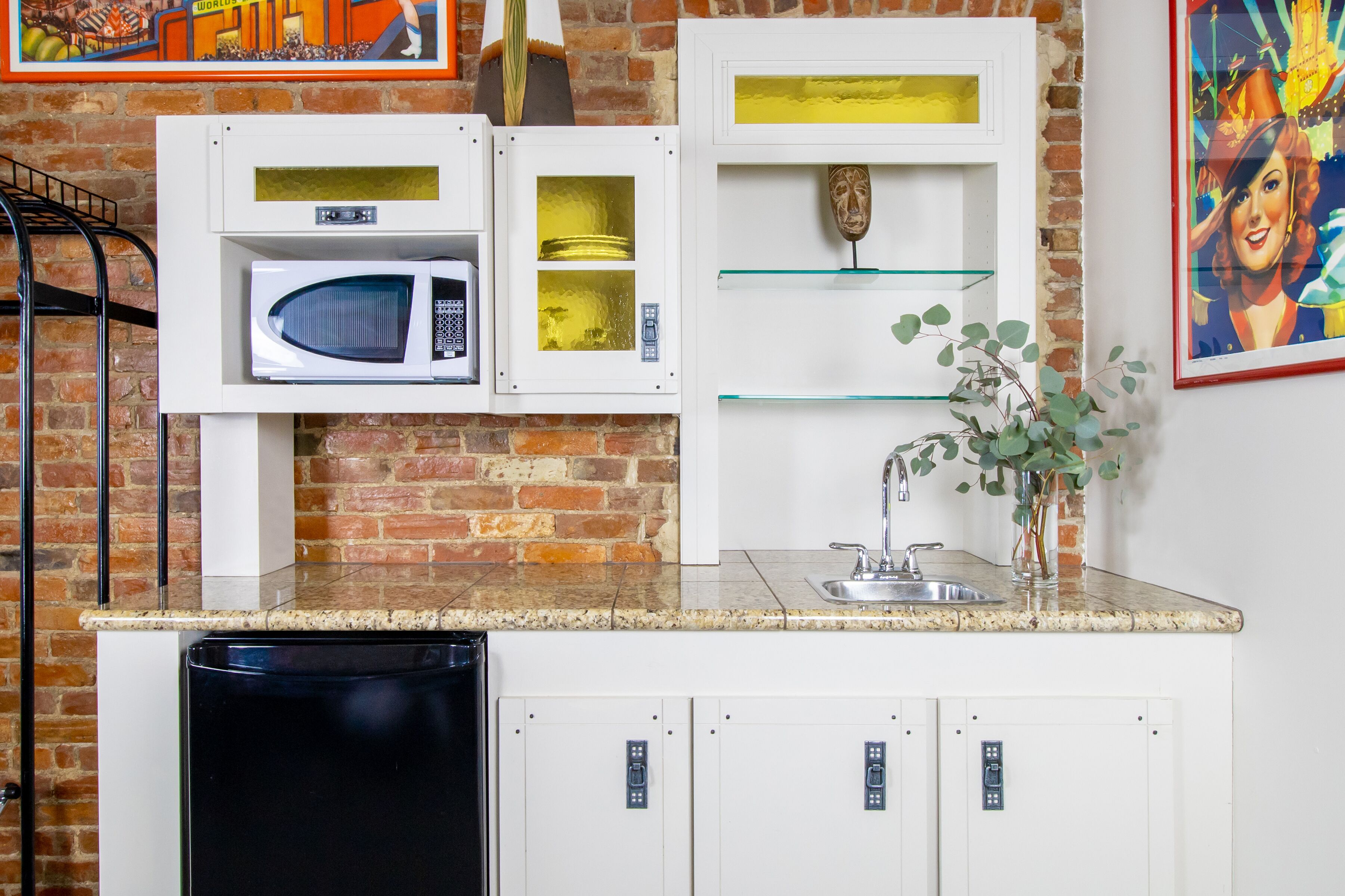 A compact kitchen with a microwave, a glass shelf, and a sink.