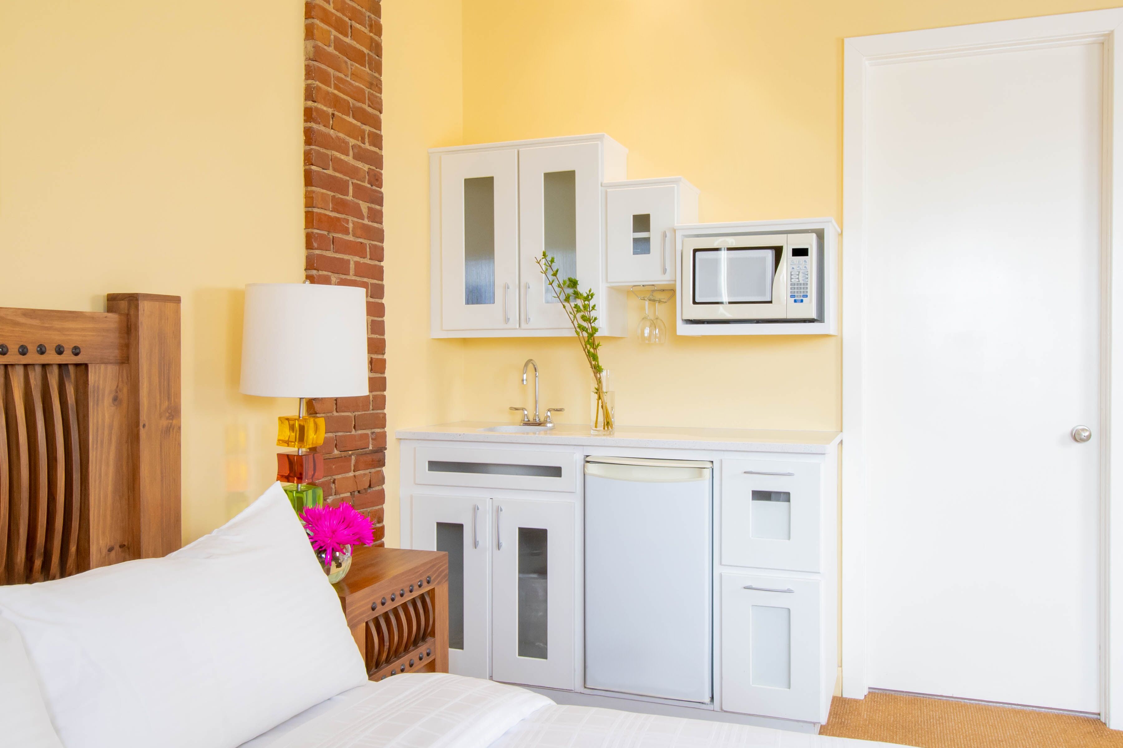A hotel room with a bed, a wooden headboard, a white cabinet with a microwave, and a brick wall.