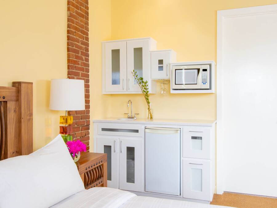 A hotel room with a bed, a wooden headboard, a white cabinet with a microwave, and a brick wall.