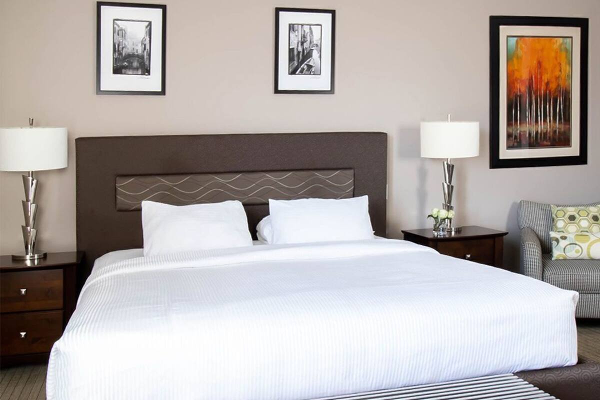 A hotel room with a large bed, two bedside tables with lamps, a bench at the foot of the bed, and three framed pictures on the wall.