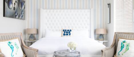 A hotel room with a large bed, two armchairs, a small round table, and a decorative pillow.