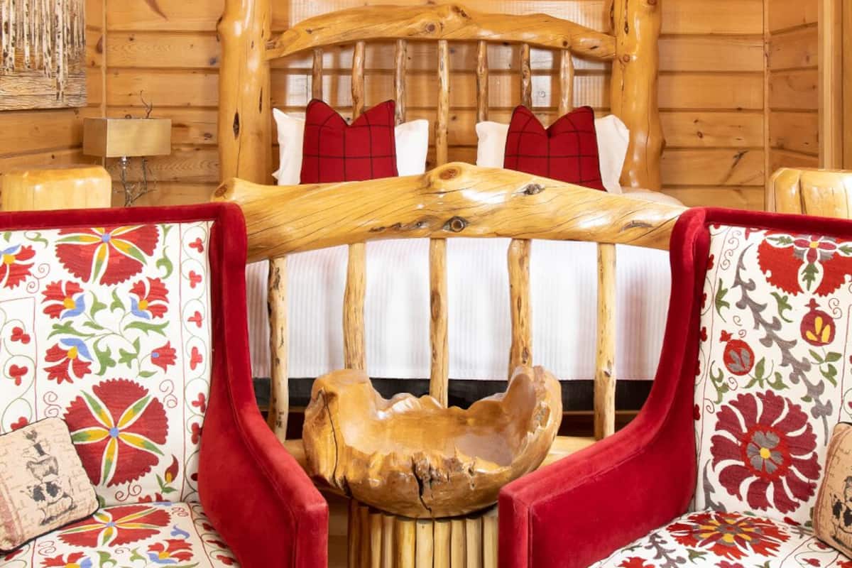 A wooden cabin bedroom with a bed, a wooden headboard, a chandelier, and three deer head wall art pieces.