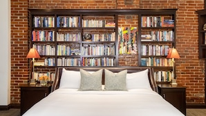 Una habitación de hotel con una cama grande, dos mesitas de noche, una estantería y una pared de ladrillo.