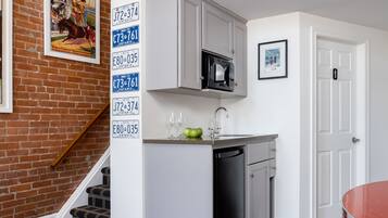 Una cocina compacta con muebles blancos, un microondas y un lavamanos. Una escalera conduce a un área tipo loft con barandilla roja.