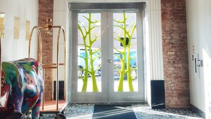 Un vestíbulo de hotel con pared de ladrillo, una puerta de entrada grande con diseños de árboles, una escultura colorida y una alfombra estampada.