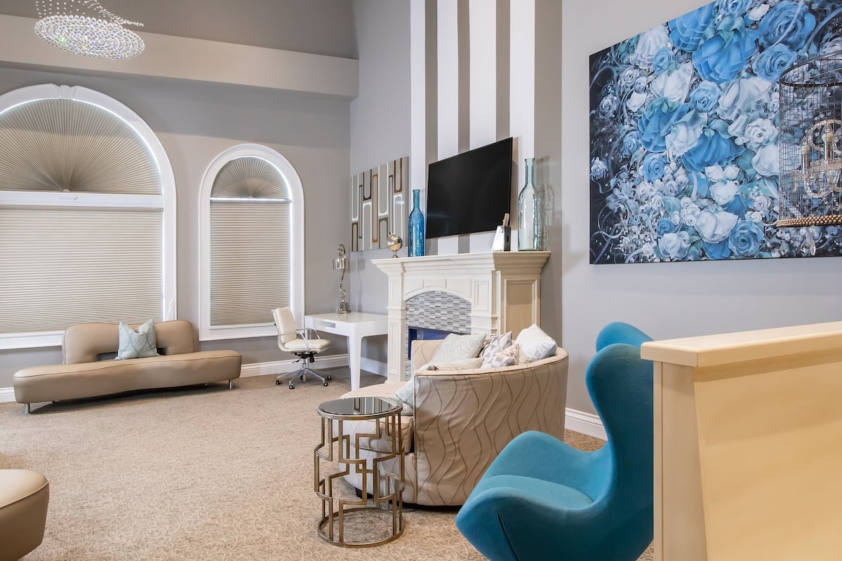 A modern living room with a beige sofa, a blue armchair, a small round table, and a fireplace with decorative items.