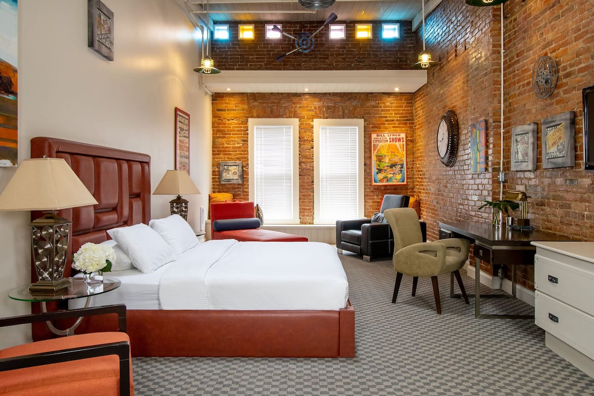 A hotel room with a large bed, two armchairs, a desk, and a brick wall.
