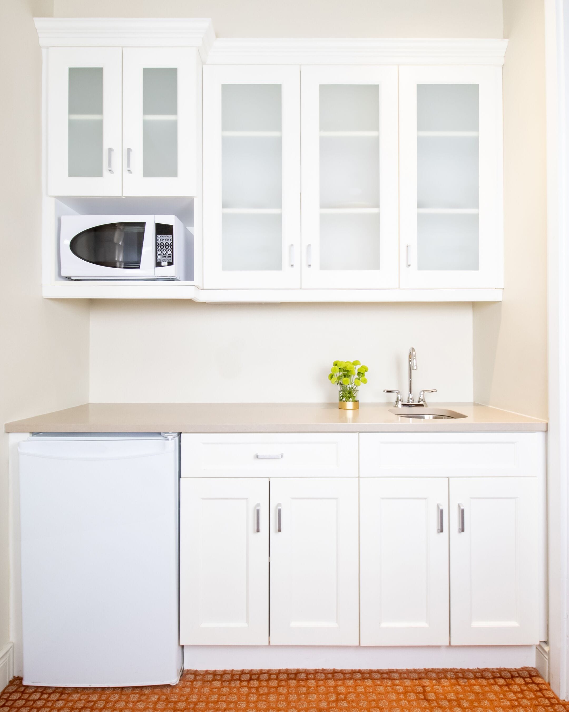 A compact kitchen with white cabinets, a microwave, a sink, and a small refrigerator.