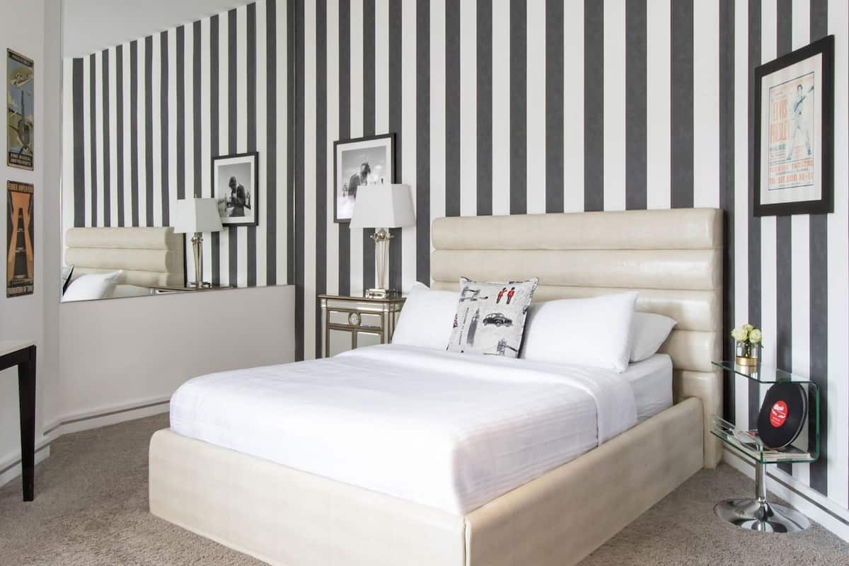 A hotel room with a large bed, a bedside table with a lamp, a mirror, and striped wallpaper.