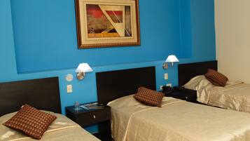 Habitación de hotel con dos camas, cada una con almohada y mesita de noche. Se observa un cuadro en la pared y una lámpara sobre cada mesita.