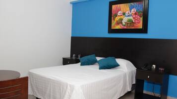 Een hotelkamer met een bed, twee nachtkastjes, een stoel en een kleurrijk schilderij aan de muur.