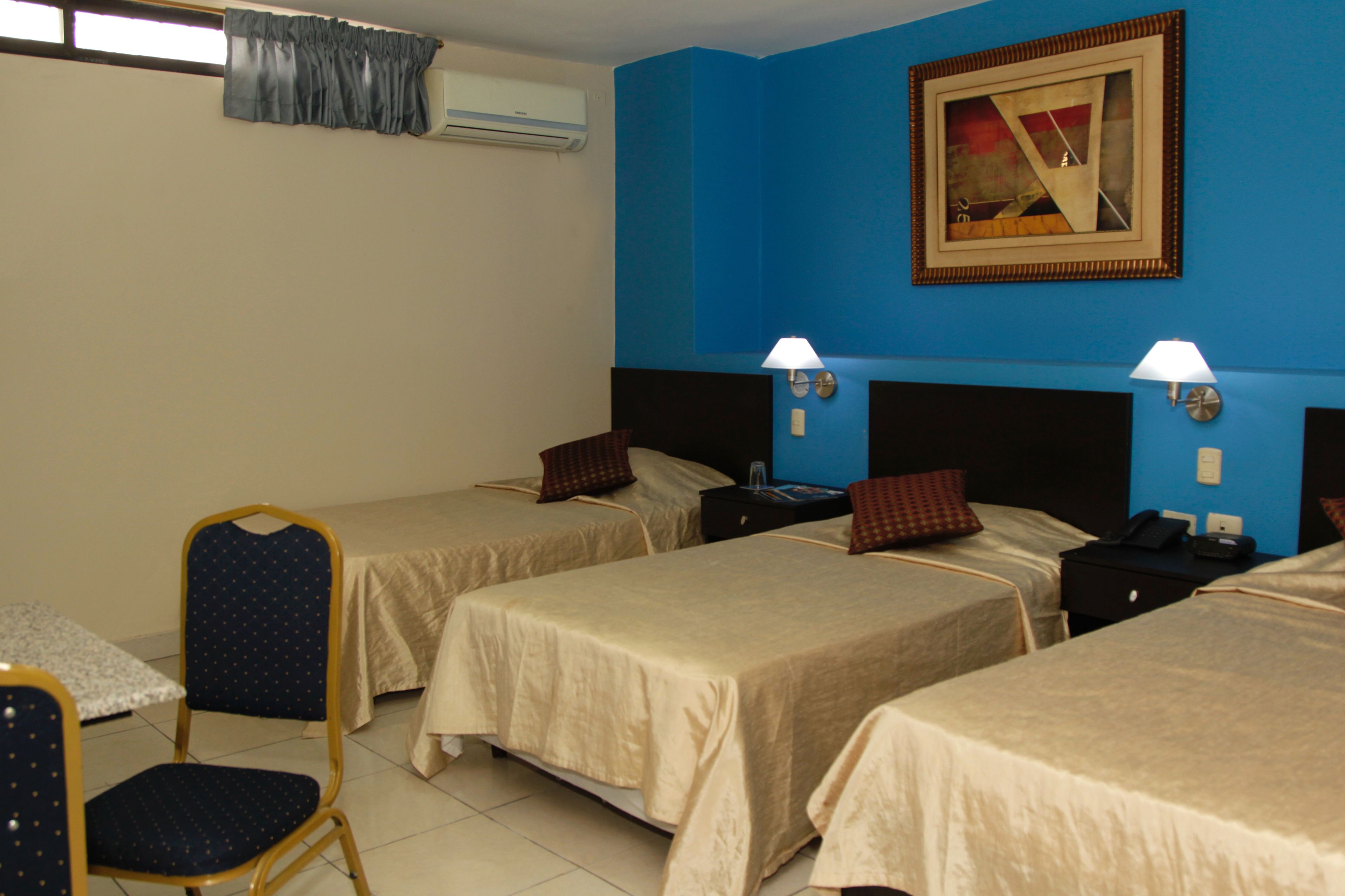 Habitación de hotel con tres camas individuales, una mesita y una silla.