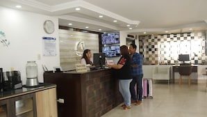 Zona de recepción de un hotel con mostrador de check-in, varias pantallas y una máquina de café.