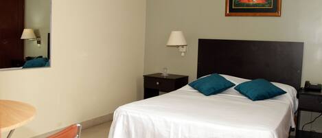 Habitación de hotel con cama, escritorio, silla, mesita de noche y un cuadro en la pared.
