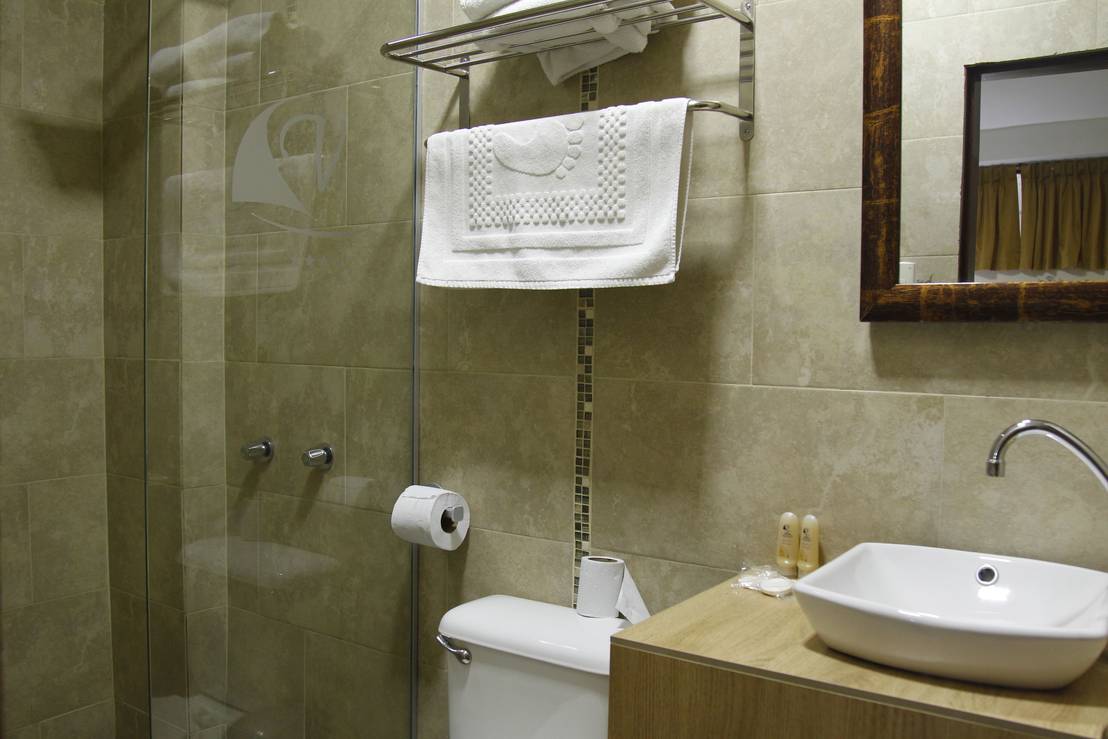 A bathroom with a glass shower enclosure, a toilet, a sink with a mirror above it, and a towel rack with a towel.