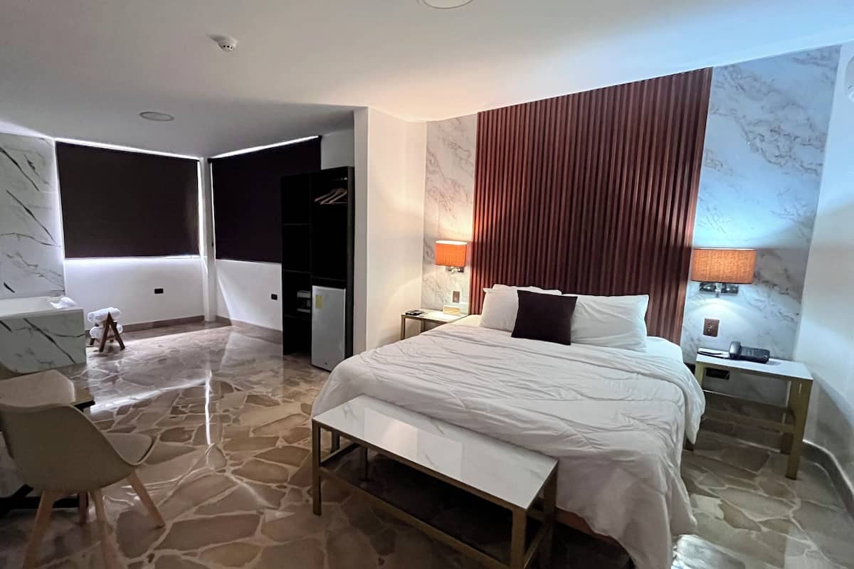 Une chambre d’hôtel comprenant un lit, des tables de chevet, un bureau, une chaise, une armoire et une petite table sur laquelle est posé un ours en peluche.