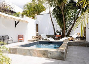 Un área de piscina con sillas de descanso, una mesita y una estructura con techo de paja.