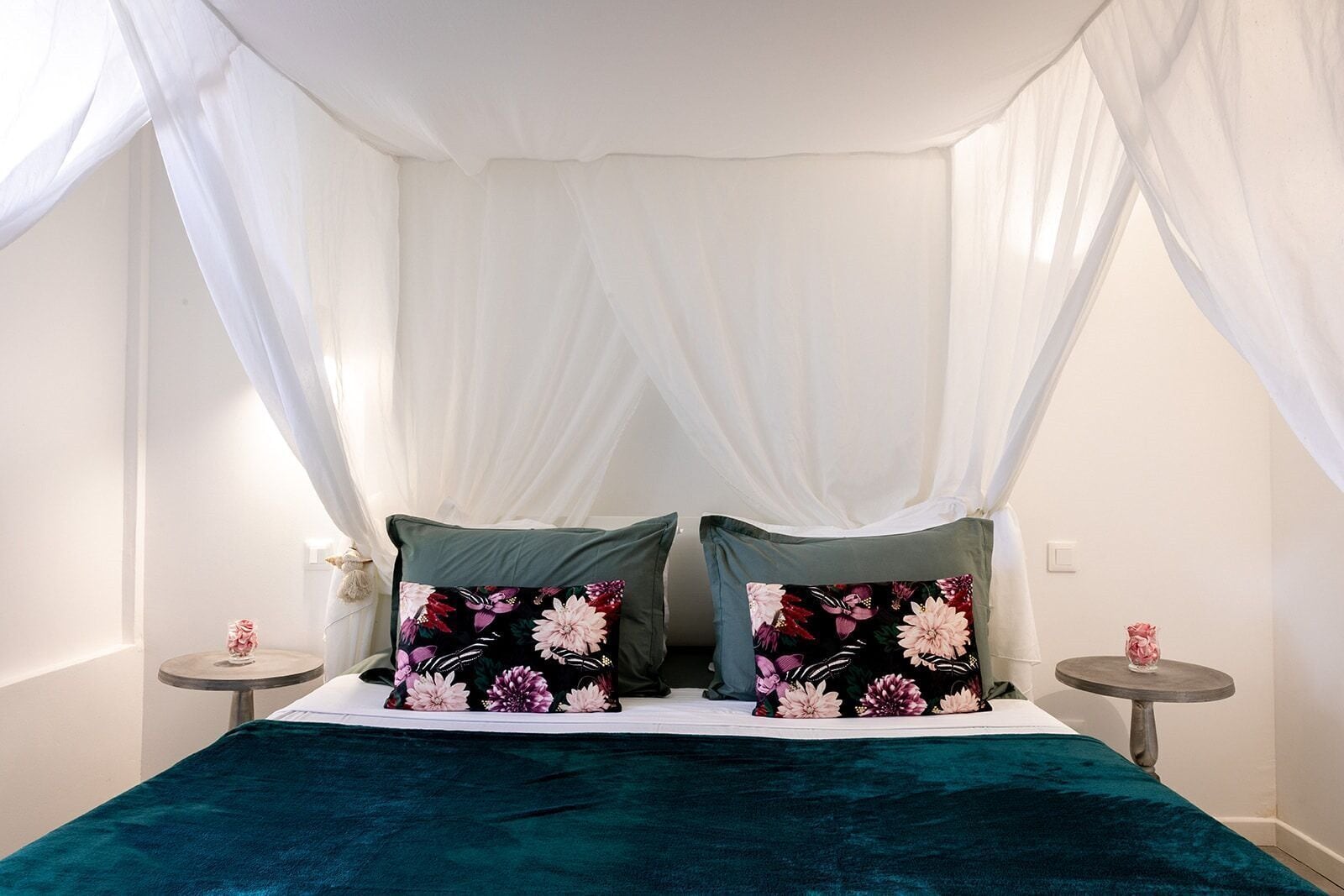 Una cama con dosel, dos almohadas con motivos florales y una colcha color turquesa.