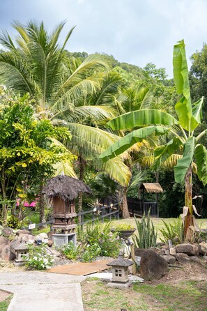 Un jardín tropical con palmeras, una estructura de techo de paja y un farol de piedra.