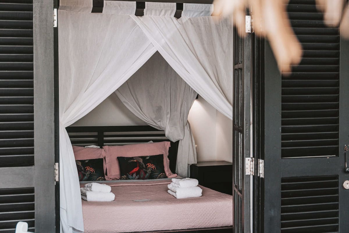 Una habitación con una cama bajo un dosel, una silla y una puerta.