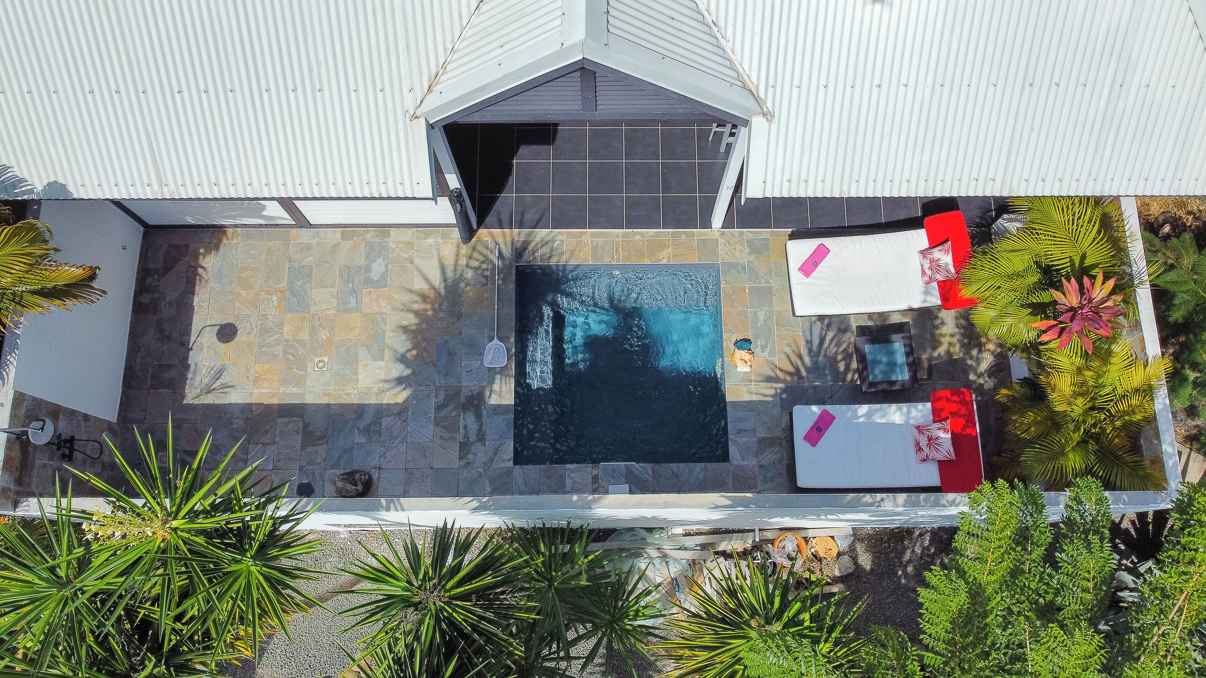 An aerial view of a rooftop with a swimming pool, surrounded by stone tiles and greenery.