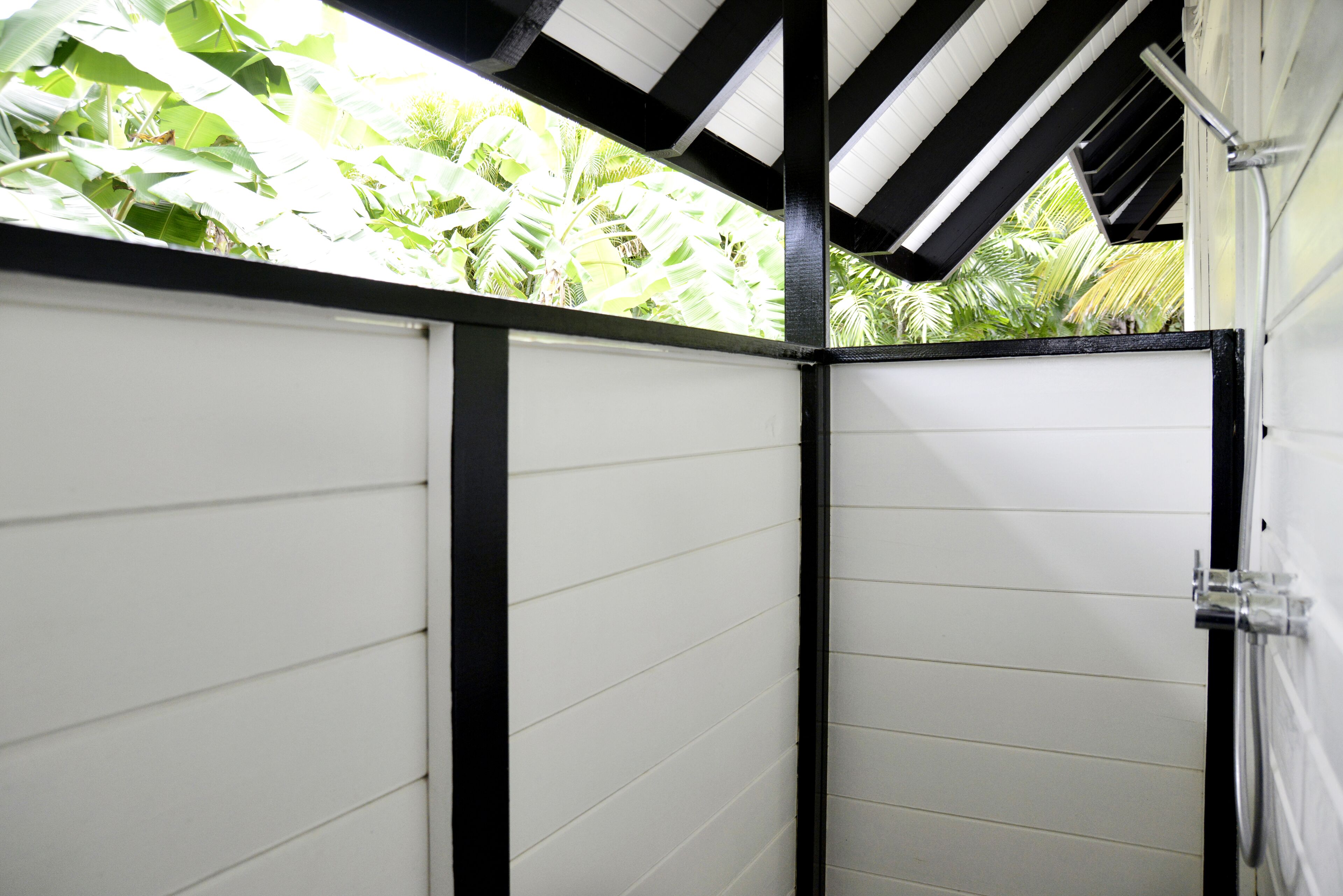 Una habitación con paredes blancas y detalles en negro, con un ventanal que ofrece vistas de frondosa vegetación.