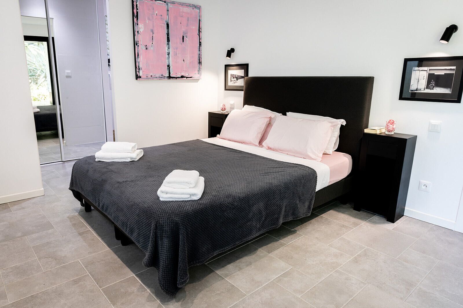 A modern bedroom with a large bed, a nightstand, and a wall-mounted lamp.