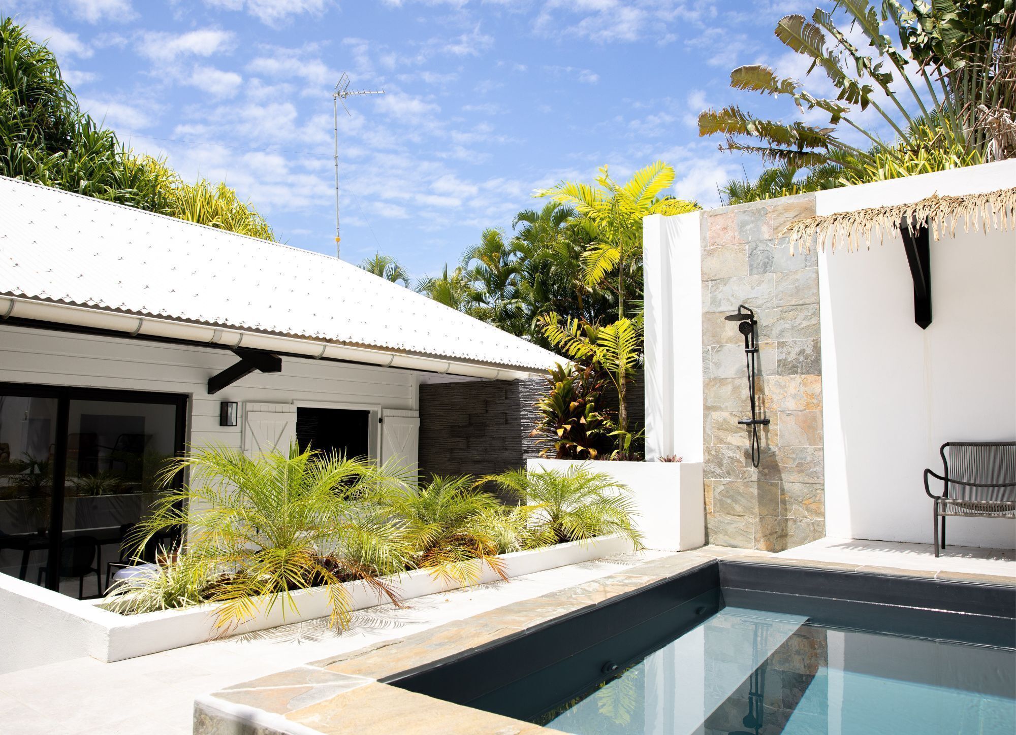A modern outdoor pool area with a stone wall, a shower, and a chair.