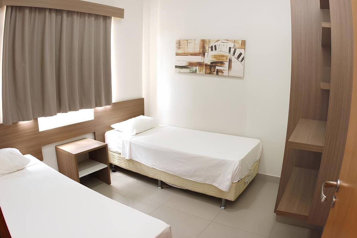 A hotel room with two single beds, a wooden nightstand, a desk, and a wardrobe.