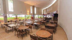 A spacious indoor dining area with multiple tables and chairs, large windows, and a view of the outdoor garden. - Hotel Marina - Oficial (Caldas Novas)