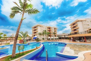 A swimming pool with a palm tree, surrounded by a multi-story building with balconies and outdoor seating.